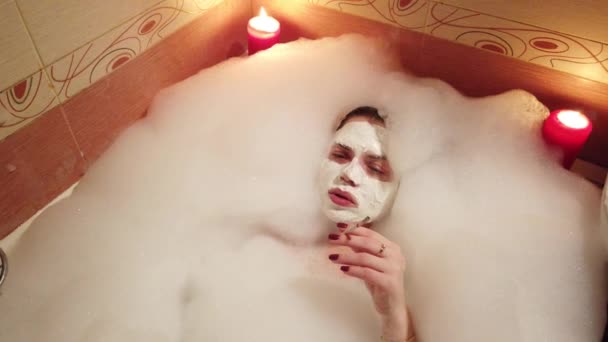 泡でいっぱいの浴室で吸うタバコの顔に粘土のマスクを持つ少女 - 映像、動画