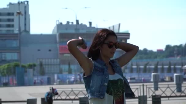 tattooed hot self-confident brunette lady take on her modern earphones in the front of urban buildings - Filmati, video