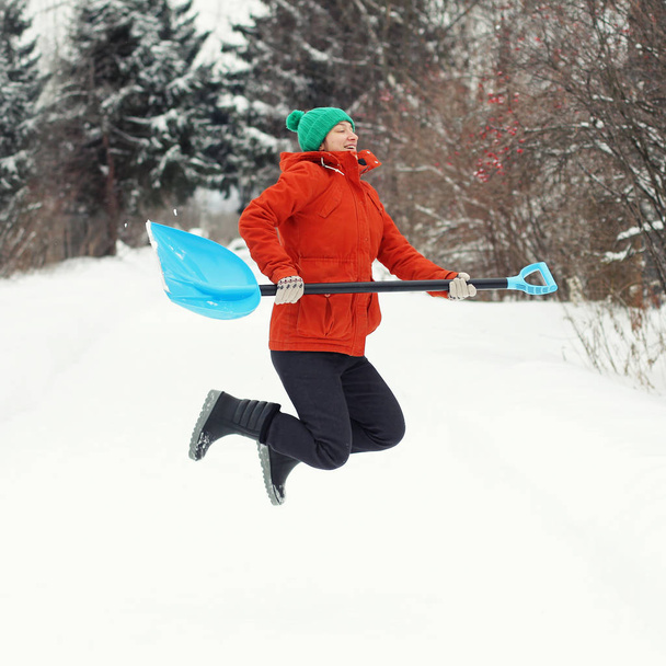 Funny young woman jump with snow shovel on rural road. Winter seasonal concept. Square. - Photo, image