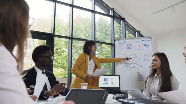 Young businesswoman conducts presentation using whiteboard on which shows the graphs buying and selling company, caucasian businesswoman gives presentation in office - Imágenes, Vídeo