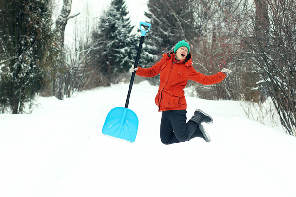 Funny young woman jump with snow shovel on rural road. Winter seasonal concept.  - Photo, image