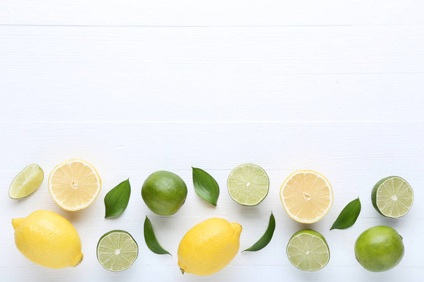 Lemons and limes with green leafs on white wooden table - Foto, afbeelding