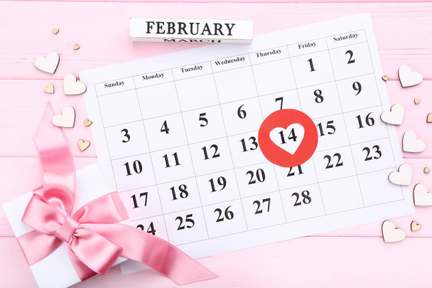 Valentine day calendar with wooden hearts and gift box on pink table - Photo, Image