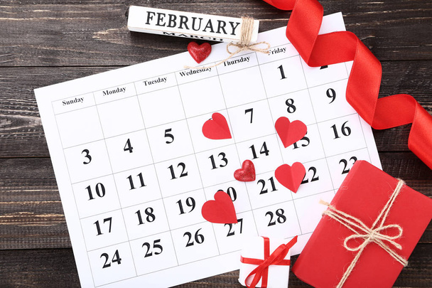 Valentine day calendar with red hearts and gift boxes on wooden table - 写真・画像