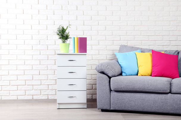 White bedside table near grey sofa and colorful pillows on brick wall background - Photo, Image
