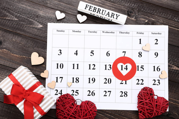 Valentine day calendar with hearts and gift box on wooden table - Photo, image