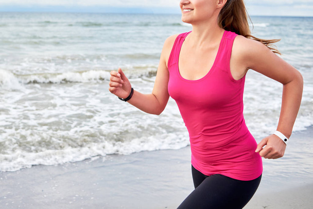 Young fitness woman runner running at seaside, copy space. Girl working out on beach at summer morning. Healthy lifestyle concept - Photo, Image