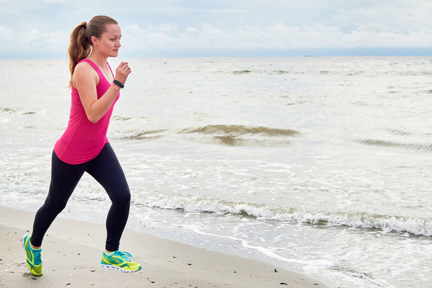 Athletic woman running on sea beach, copy space. Female runner working out at summer morning, full length body portrait. Healthy lifestyle concept - Photo, Image
