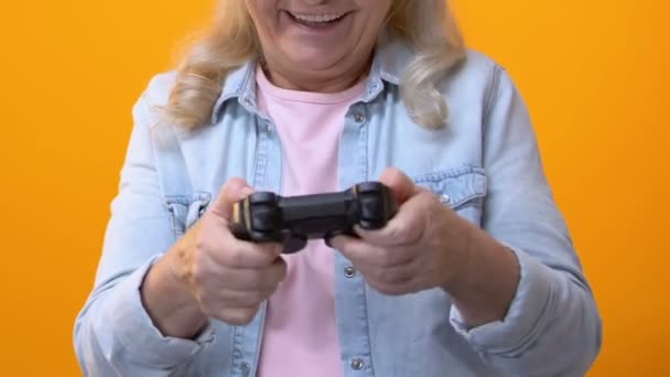Excited granny playing video game by joystick on bright background, leisure fun - 映像、動画