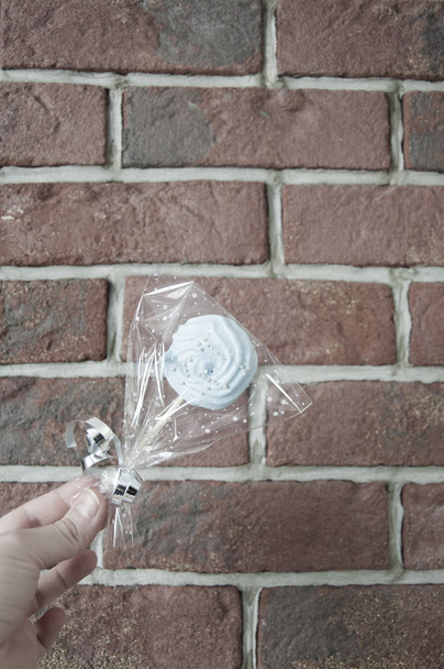 merengue en paquete en mano femenina sobre fondo de pared de ladrillo, espacio de copia. cumpleaños y regalo de fiesta de Pascua o Navidad
 - Foto, imagen
