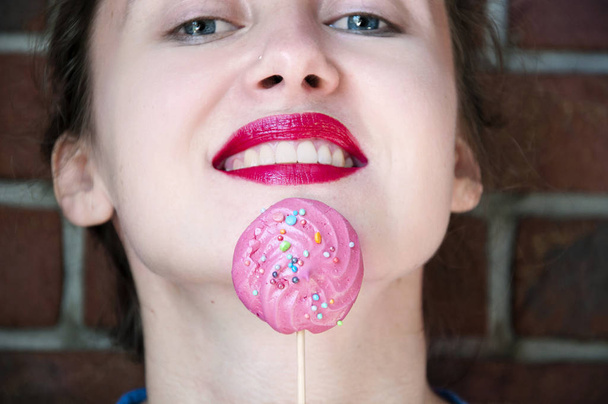 Красотка-манекенщица с эффектным макияжем, принимающая красочные меренги lollipop. Красивая женщина, яркий макияж. Фиолетовая помада. Диета, диета. Свитс
. - Фото, изображение