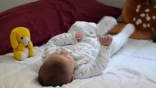 niedlichen Baum Monate alten Jungen in weiß gekleidet, auf weißen Bettdecke treten mit den Füßen und machen lustige Gesichter - Filmmaterial, Video