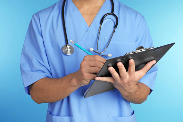 Male doctor with stethoscope and clipboard on color background, closeup. Medical objects - Foto, Imagem