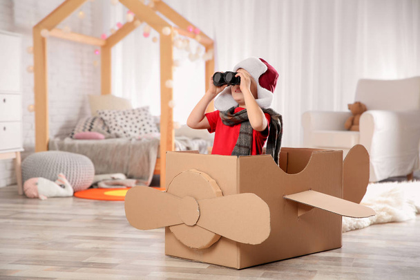 Cute little boy playing with binoculars and cardboard airplane in bedroom - Photo, Image