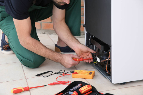 Male technician repairing broken refrigerator indoors, closeup - 写真・画像