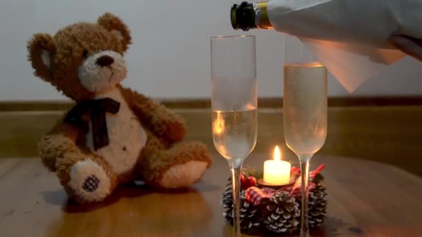 Hombre vertiendo champán en vidrio, sobre mesa de madera con oso de peluche detrás
  - Imágenes, Vídeo