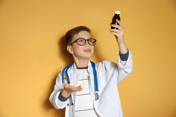 Cute little child in doctor coat with medication on color background - Foto, afbeelding
