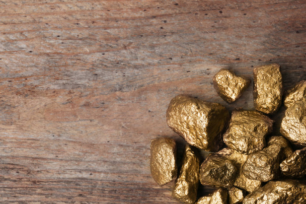 Pile of gold nuggets on wooden background, top view with space for text - Foto, imagen