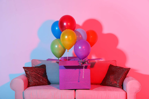 Gift box with bright air balloons on sofa against color background - Foto, Imagem