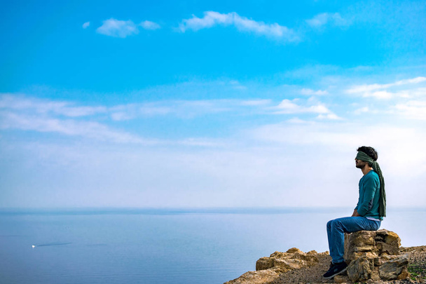 Молодой человек с повязкой на глазах на вершине утёса над морским пейзажем
 - Фото, изображение