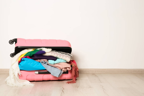 Suitcase with clothes for winter vacation on floor against white wall. Space for text - Foto, afbeelding