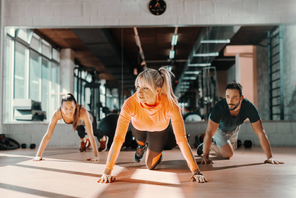 Grupa sportowa osób zdrowych nawyków ćwiczeń siły na podłodze sali gimnastycznej. W tle lustro. - Zdjęcie, obraz