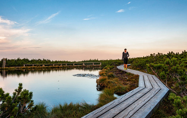 woman walking on wooden path next to a small lake - Photo, Image