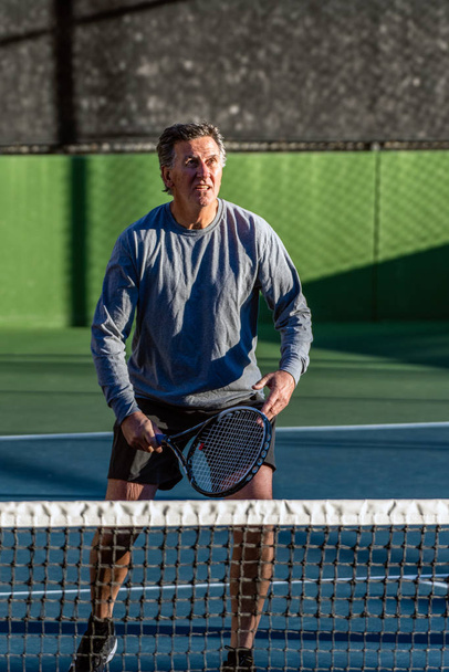 Skupiony i starszych rekreacyjnych tenisista szukają okazji, aby uderzyć piłkę podczas gry w tenisa. - Zdjęcie, obraz
