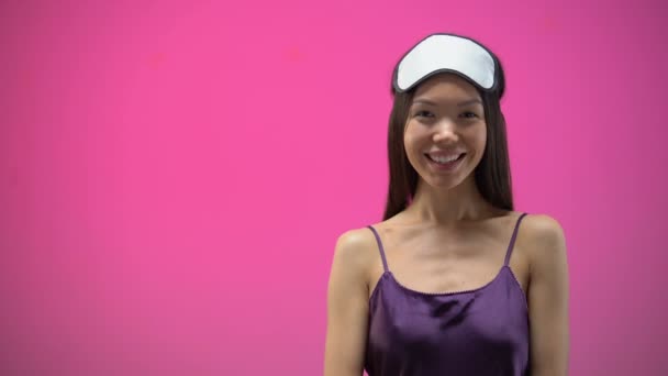 Asian girl in pajamas and eye mask blowing confetti, isolated on pink background - Imágenes, Vídeo