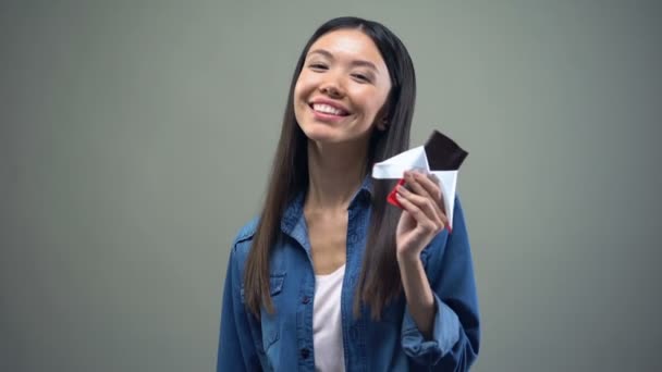 Attractive asian girl smiling on camera eating dark chocolate, advertisement - Filmagem, Vídeo