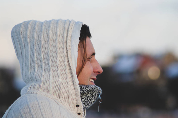 Close up portrait of a middle aged man wearing a hooded white knitting jacket in cold and windy weather and looking into the distance. Winter time in Riga, Latvia - Photo, Image