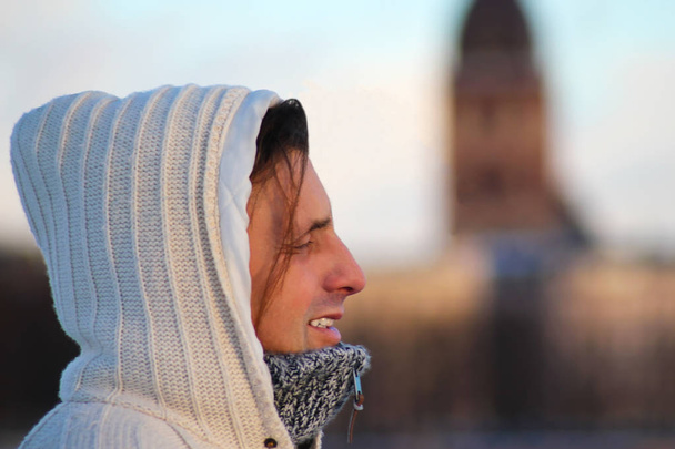 Bir orta portre yakından Örgü ceket soğuk ve rüzgarlı havalarda ve mesafe içine bakarak bir kukuletalı beyaz giyen adam yaşlı. Kış döneminde Riga, Letonya - Fotoğraf, Görsel
