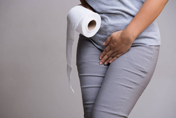 Frau Hand hält ihren Schritt Unterbauch und Taschentuch oder Toilettenpapierrolle. Durchfall, Inkontinenz. Gesundheitskonzept. - Foto, Bild
