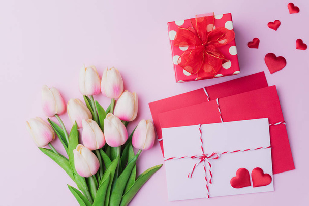 Ystävänpäivä ja rakkauden käsite. Vaaleanpunainen tulppaanit, lahja laatikko punainen sydän ja punainen vaaleanpunainen kirjekuori vaaleanpunainen tausta
. - Valokuva, kuva