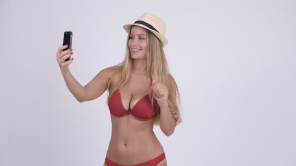 Happy young blonde tourist woman in bikini video calling with phone - Záběry, video