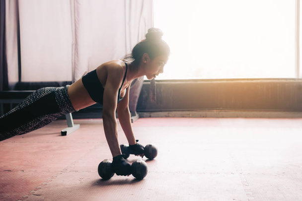 Young asian woman doing push-ups on dumbbell in a gym. - Photo, Image