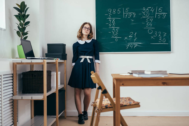 Sad schoolgirl standing in front of blackboard. - Zdjęcie, obraz