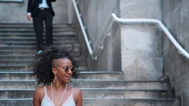 Μοντέρνα νεαρή μαύρη γυναίκα φοράει γυαλιά ηλίου περπατώντας κάτω από σκάλες σε δρόμο της πόλης - Πλάνα, βίντεο