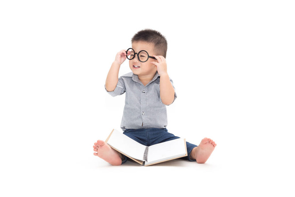 Bonito criança brinca com livro e usando óculos enquanto sentado no chão isolado sobre fundo branco, menino asiático e conceito de educação
 - Foto, Imagem