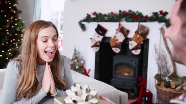 Man handing Christmas gift to woman who trying to guess contents as they celebrating at home together - shot in slow motion - Imágenes, Vídeo