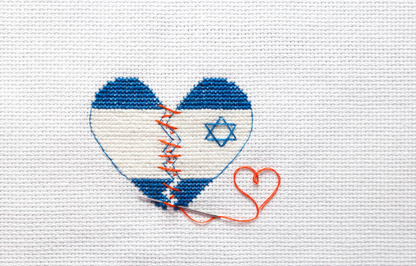 Κεντήστε την σπασμένη καρδιά από τα χρώματα της σημαίας του Ισραήλ που έραβαν με κόκκινα νήματα. Εγχείρηση καρδιάς. - Φωτογραφία, εικόνα