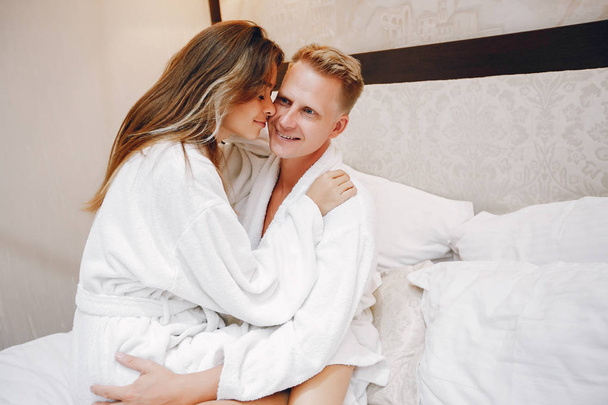 Loving couple sitting on a bed. Man and woman in a white bathrobes - Φωτογραφία, εικόνα