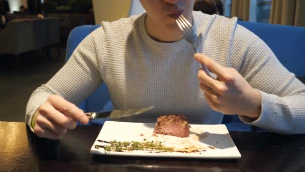 Člověk jíst steak s vidličkou a nožem v kavárně rychlého občerstvení na večer - Záběry, video