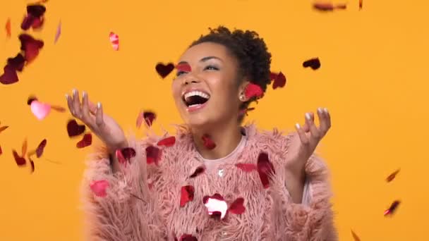 Joyful american woman standing under falling heart-shaped confetti, valentine - Πλάνα, βίντεο