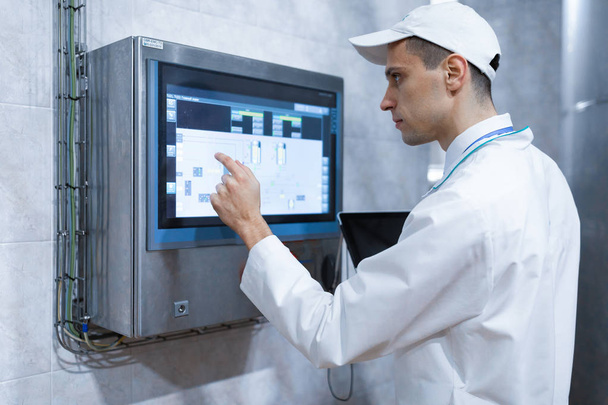 Tecnólogo con un portátil en las manos cerca del monitor de la planta láctea
 - Foto, imagen