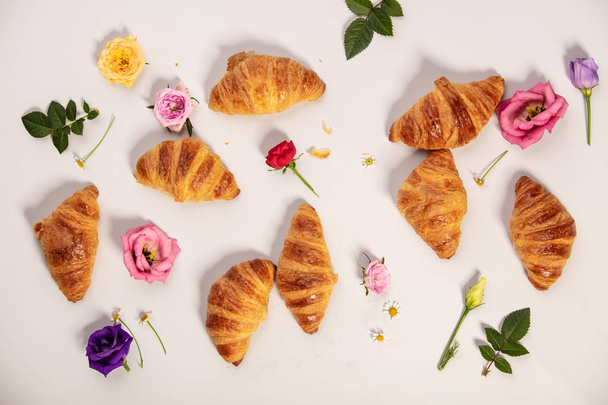 Delicious fresh mini croissants and flowers on white background, flat lay, minimalistic style - Photo, image