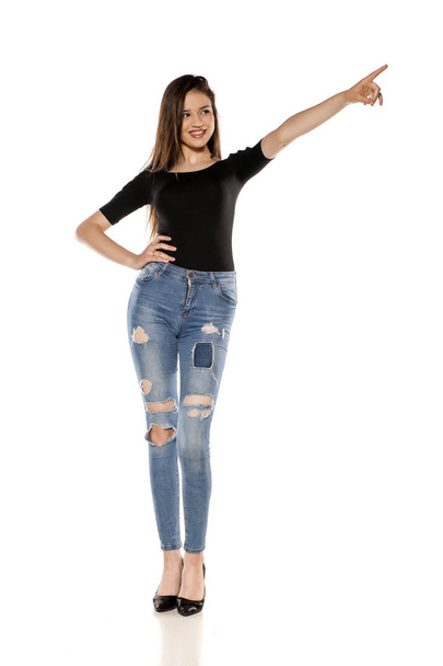 Happy young girl in ripped jeans pointing on a white background - Photo, Image