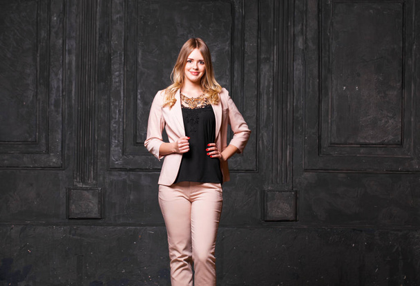 Fashion portrait of pretty sexy young blonde woman in pink pantsuit posing on dark wall background  - Foto, imagen