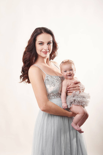 jonge aantrekkelijke moeder met een klein meisje op een lichte achtergrond - Foto, afbeelding
