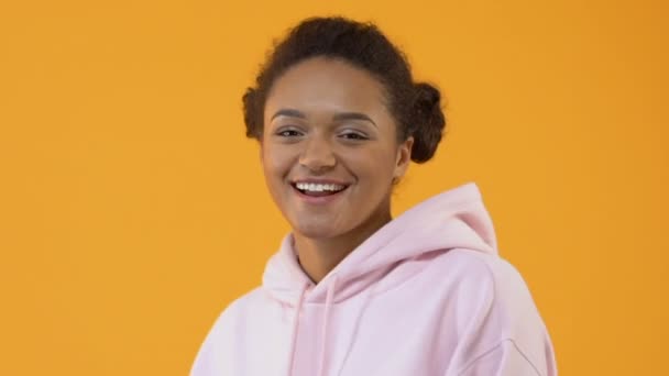 Joyful female teenager in stylish pink hoodie smiling camera yellow background - Кадры, видео